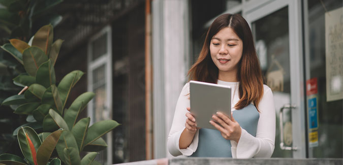 A young woman smiles while looking at her tablet. 