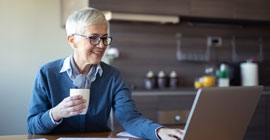 A woman holds a mug while working on her laptop.